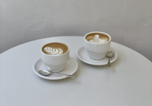 Two lattes in white coffee cups on a round white table